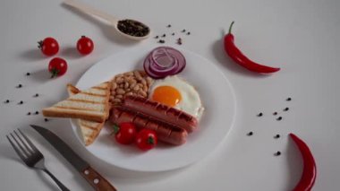 İngiliz Kahvaltısı. Kızarmış yumurta, iki kızarmış sosis, kızarmış ekmek tostu, konserve fasulye, mavi soğan ve beyaz arka planda vişneli domates. İngiliz kahvaltısı konsepti. Kapat.