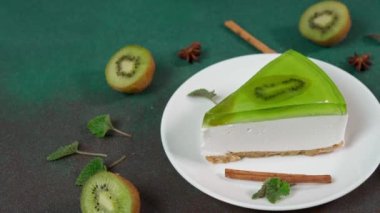 Dilimlenmiş Cheesecake 'i Kiwi ile kapat. Bir dilim kivi, tarçın çubuğu, badyan ve nane yapraklarıyla süslenmiş.