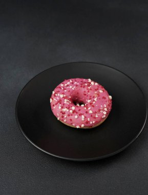 Siyah bir tabakta renkli serpiştirilmiş pembe jöleli çörek. Siyah arka planda pembe çörek.