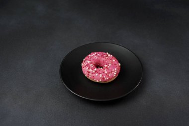 Siyah bir tabakta renkli serpiştirilmiş pembe jöleli çörek. Siyah arka planda pembe çörek.