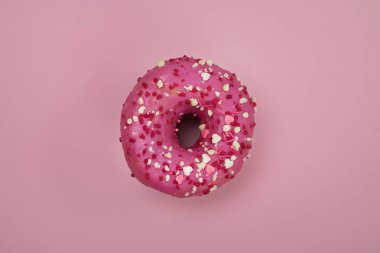Pembe arka planda renkli serpiştirilmiş pembe bir çöreğin üst görüntüsü. Pembe arka planda pembe çörek.