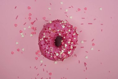 Pembe arka planda renkli serpiştirilmiş pembe bir çöreğin üst görüntüsü. Pembe arka planda pembe çörek.