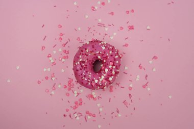 Pembe arka planda renkli serpiştirilmiş pembe bir çöreğin üst görüntüsü. Pembe arka planda pembe çörek.