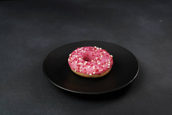 Pink glazed Doughnut with colorful sprinkles on a black plate. Pink donut on a black background