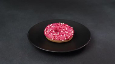 Siyah bir tabakta renkli serpiştirilmiş pembe jöleli çörek. Siyah arka planda pembe çörek.