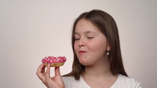 Gadis Kaukasia Dengan Kaos Putih Makan Donut Tangannya Dengan Glasir — Stok Video