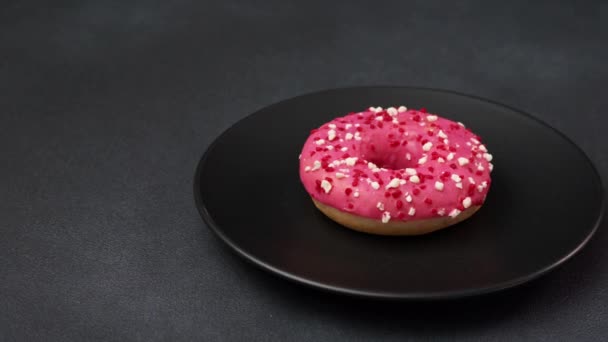 Rosa Glasierter Donut Mit Bunten Streusel Auf Einem Schwarzen Teller — Stockvideo