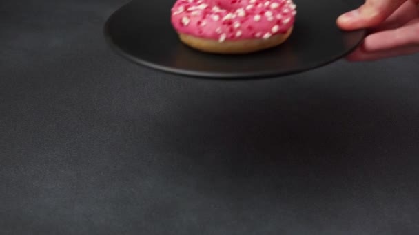Рука Кавказца Кладет Черную Тарелку Розовым Глазурованным Пончиком Стол Розовый — стоковое видео