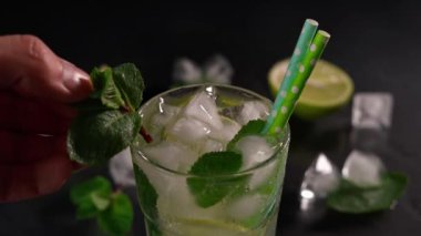 Naneli Mojito kokteyli süsleyen bir barmenin elinin yakın çekimi. Buzlu kokteyl ve siyah arka planda yeşil nane yaprakları.