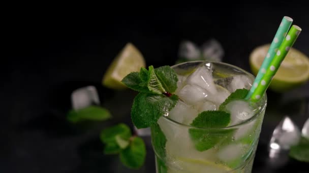 用石灰 冰块和绿色薄荷叶在黑色背景上重新装饰莫吉托鸡尾酒的特写 — 图库视频影像