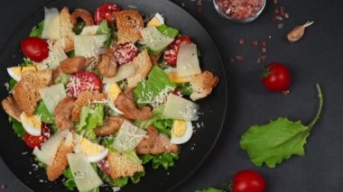 Tavuklu Sezar Salatası, marul yaprakları, kiraz domatesleri, siyah bir tabakta rendelenmiş parmesan.