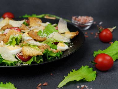Tavuklu Sezar Salatası, marul yaprakları, kiraz domatesleri, siyah bir tabakta rendelenmiş parmesan.