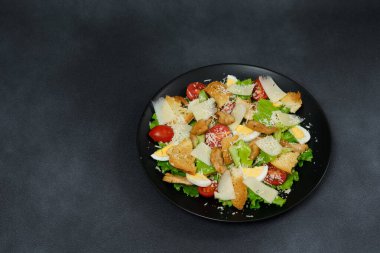 Tavuklu Sezar Salatası, marul yaprakları, kiraz domatesleri, siyah bir tabakta rendelenmiş parmesan...