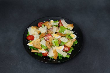 Tavuklu Sezar Salatası, marul yaprakları, kiraz domatesleri, siyah bir tabakta rendelenmiş parmesan...