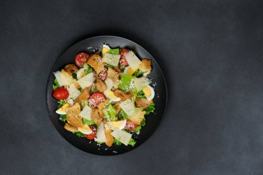 Tavuklu Sezar salatası, marul yaprakları, kiraz domatesleri, siyah bir tabakta rendelenmiş parmesan.