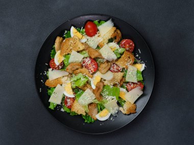 Tavuklu Sezar salatası, marul yaprakları, kiraz domatesleri, siyah bir tabakta rendelenmiş parmesan.