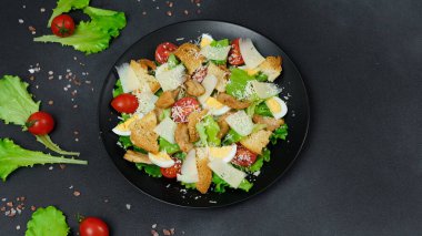 Tavuklu Sezar Salatası, marul yaprakları, kiraz domatesleri, siyah bir tabakta rendelenmiş parmesan...
