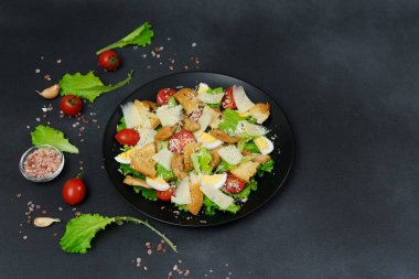 Tavuklu Sezar salatası, marul yaprakları, kiraz domatesleri, siyah bir tabakta rendelenmiş parmesan.