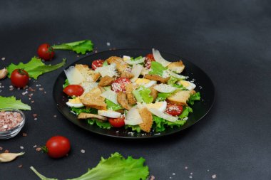 Tavuklu Sezar Salatası, marul yaprakları, kiraz domatesleri, siyah bir tabakta rendelenmiş parmesan...