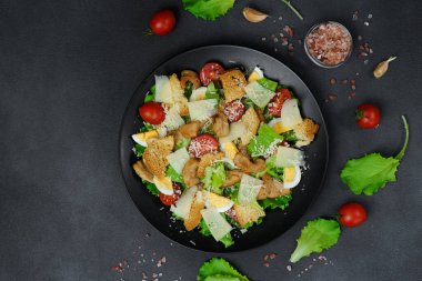 Tavuklu Sezar salatası, marul yaprakları, kiraz domatesleri, siyah bir tabakta rendelenmiş parmesan.
