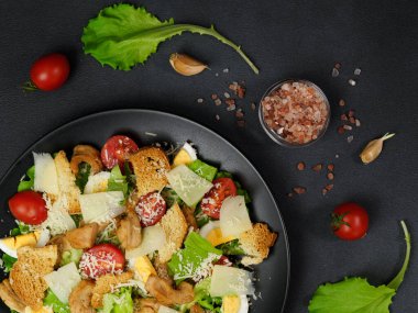 Tavuklu Sezar salatası, marul yaprakları, kiraz domatesleri, siyah bir tabakta rendelenmiş parmesan.