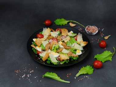 Tavuklu Sezar Salatası, marul yaprakları, kiraz domatesleri, siyah bir tabakta rendelenmiş parmesan...