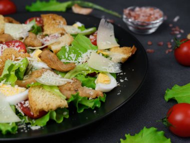 Tavuklu Sezar Salatası, marul yaprakları, kiraz domatesleri, siyah bir tabakta rendelenmiş parmesan.