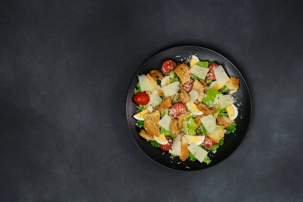 一张凯撒沙拉的头像 上面有鸡肉 莴苣叶 樱桃西红柿 黑盘子里的烤意大利面和黑色背景 — 图库照片