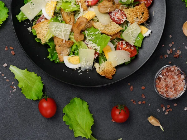 鶏とシーザーサラダのトップビュー レタスの葉 チェリートマト 黒の背景に黒いプレートにすりおろしたパルメザン — ストック写真