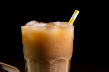 Kapuçinonun kapuçinosu, uzun bir bardakta buzla kaplanmış, siyah bir arka planda. Sütlü buzlu kahve.