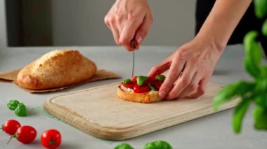 Elleri bıçakla kesilmiş, Ricotto peyniri ve ahşap kesim tahtasının üstünde domates ızgarası. Ricotto peynirli, kirazlı, domatesli, fesleğenli, sarımsaklı gri beton arka planda