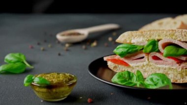 Jambonlu Ciabatta Sandviçi, Pesto sosu, Domates, siyah arka planda Basil. Yiyecekler. Yemek arkaplanı. Yakın plan.