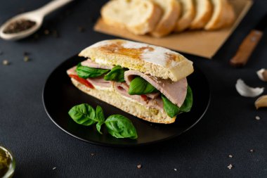 Jambonlu Ciabatta Sandviçi, Pesto sosu, Domates, siyah arka planda Basil. Yiyecekler. Yemek arkaplanı. Yakın plan.