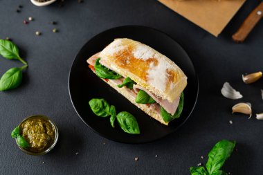 Jambonlu Ciabatta Sandviçi, Pesto sosu, Domates, siyah arka planda Basil. Yiyecekler. Gıda arkaplanı