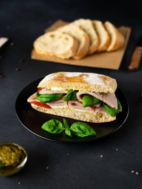 Jambonlu Ciabatta Sandviçi, Pesto sosu, Domates, siyah arka planda Basil. Yiyecekler. Yemek arkaplanı. Yakın plan.