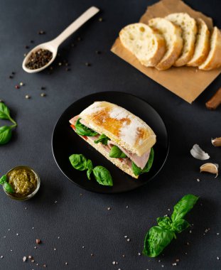 Jambonlu Ciabatta Sandviçi, Pesto sosu, Domates, siyah arka planda Basil. Yiyecekler. Yemek arkaplanı. Üst görünüm
