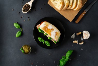 Jambonlu Ciabatta Sandviçi, Pesto sosu, Domates, siyah arka planda Basil. Yiyecekler. Yemek arkaplanı. Üst görünüm