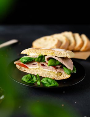 Jambonlu Ciabatta Sandviçi, Pesto sosu, Domates, siyah arka planda Basil. Yiyecekler. Yemek arkaplanı. Yakın plan.