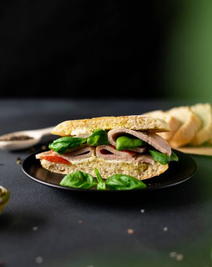Jambonlu Ciabatta Sandviçi, Pesto sosu, Domates, siyah arka planda Basil. Yiyecekler. Yemek arkaplanı. Yakın plan.