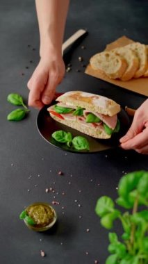 Adamın elleri masaya bir tabak Chiabatta sandviçi, jambon, fesleğen, pesto sosu ve domates koyar. Yemek arkaplanı. Dikey video
