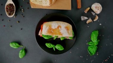 Jambonlu Ciabatta Sandviçi, Pesto sosu, Domates, siyah arka planda Basil. Yiyecekler. Yemek arkaplanı. Üst görünüm