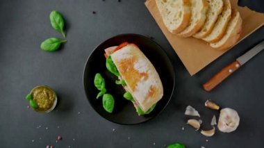 Jambonlu Ciabatta Sandviçi, Pesto sosu, Domates, siyah arka planda Basil. Yiyecekler. Yemek arkaplanı. Üst görünüm