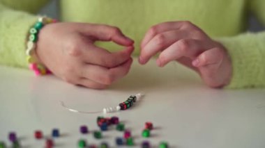 Uzun saçlı ve sarı kazaklı küçük bir kız boncuklu mücevherler örüyor.