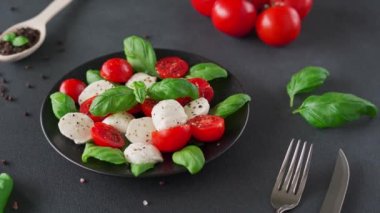 Olgun domatesli Caprese salatası ve siyah arka planda taze fesleğen yapraklı mozzarella peyniri. İtalyan yemeği. Yakın plan.