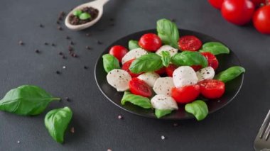 Dilimlenmiş domatesli İtalyan Caprese salatası, mozzarella peyniri, fesleğen, siyah arka planda zeytinyağı. Vejetaryen yemeği.