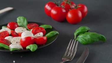 Olgun domatesli Caprese salatası ve siyah arka planda taze fesleğen yapraklı mozzarella peyniri. İtalyan yemeği. Yakın plan.