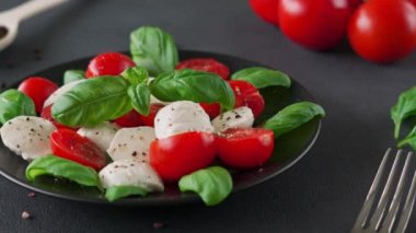 Olgun domatesli Caprese salatası ve siyah arka planda taze fesleğen yapraklı mozzarella peyniri. İtalyan yemeği. Yakın plan.