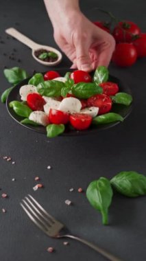 Olgun domatesli Caprese salatası ve siyah arka planda taze fesleğen yapraklı mozzarella peyniri. İtalyan yemeği. Dikey video