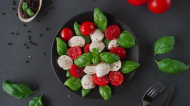 Olgun domatesli Caprese salatası ve siyah arka planda taze fesleğen yapraklı mozzarella peyniri. İtalyan yemeği.