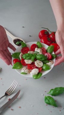 Olgun domatesli Caprese salatası ve açık arkaplanda taze fesleğen yapraklı mozzarella peyniri. İtalyan yemeği. Dikey video
